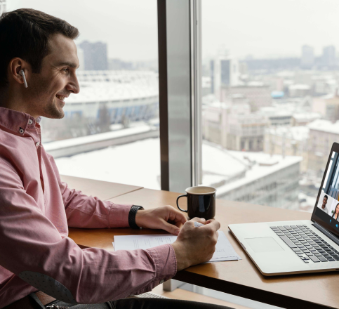 a businessman sitting at a desk with a laptop and a cup of coffee while talking with his team in an online meeting