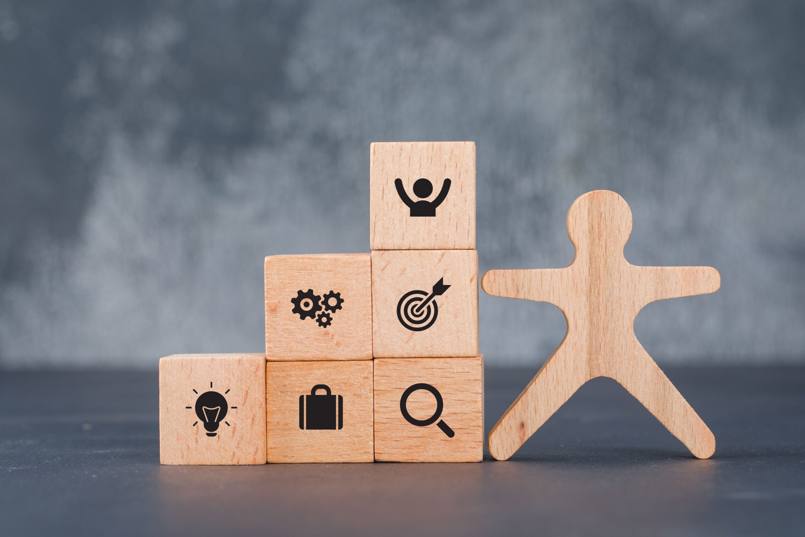 Six wooden blocks displaying business life icons near to a wooden human figure